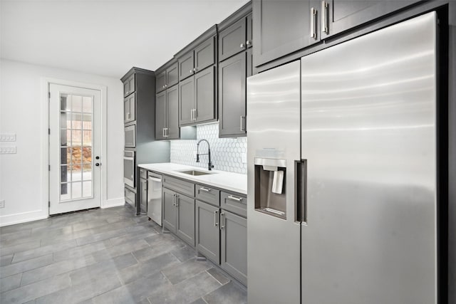 kitchen with tasteful backsplash, gray cabinets, light countertops, appliances with stainless steel finishes, and a sink