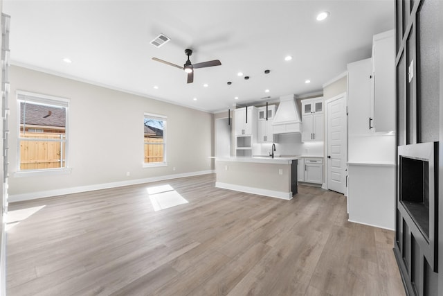 unfurnished living room with light wood-style flooring, a sink, visible vents, baseboards, and crown molding