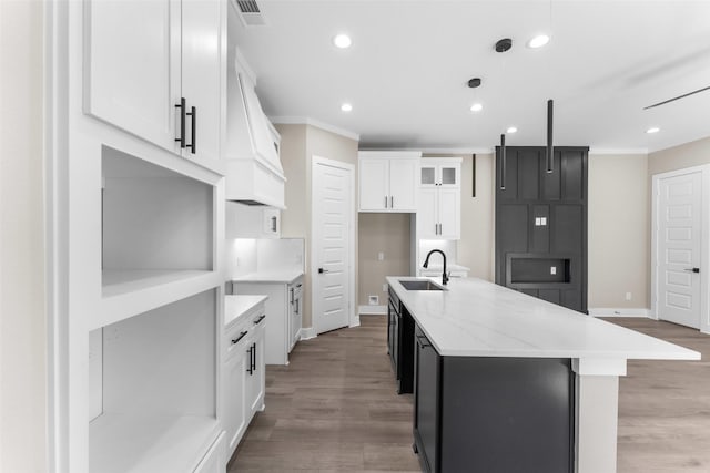 kitchen featuring visible vents, ornamental molding, a kitchen island with sink, a sink, and light wood-type flooring