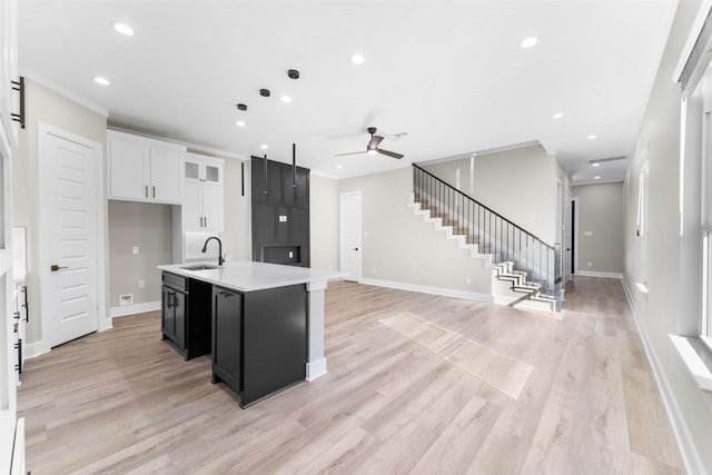 kitchen with dark cabinets, a kitchen island with sink, light countertops, white cabinetry, and a sink