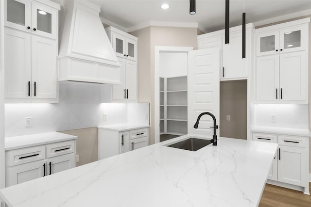 kitchen with light stone counters, custom range hood, a sink, and white cabinetry