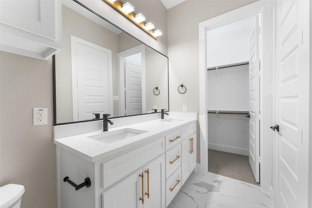 bathroom featuring marble finish floor, double vanity, a sink, and a walk in closet