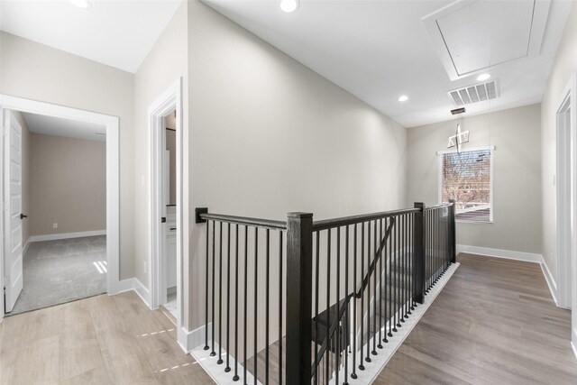 hall with attic access, baseboards, visible vents, wood finished floors, and an upstairs landing