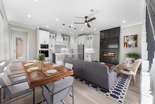 dining space with light wood-type flooring, ornamental molding, a fireplace, and visible vents