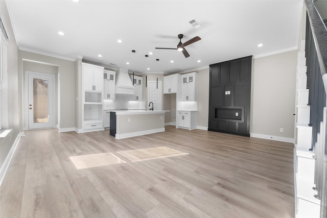 unfurnished living room featuring light wood finished floors, a sink, visible vents, and crown molding