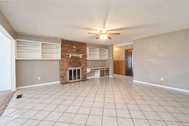 unfurnished living room with light tile patterned flooring, a brick fireplace, ceiling fan, and a textured ceiling