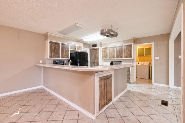 kitchen with washer / dryer, a textured ceiling, light tile patterned floors, black refrigerator, and kitchen peninsula