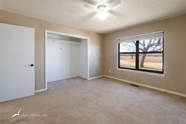 unfurnished bedroom with light carpet, a textured ceiling, a closet, and ceiling fan