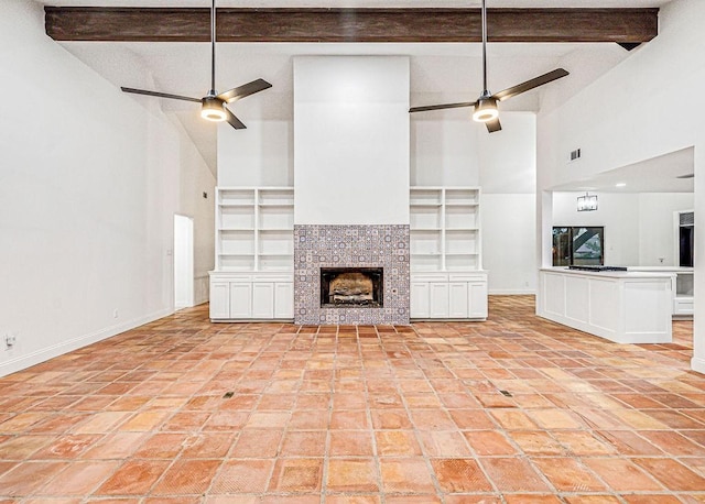 unfurnished living room featuring beam ceiling, built in features, a tile fireplace, and ceiling fan