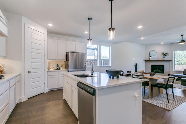 kitchen featuring sink, white cabinetry, hanging light fixtures, stainless steel appliances, and a center island with sink