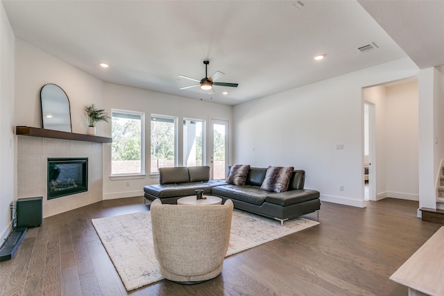 living room with dark wood-type flooring, a tile fireplace, and ceiling fan