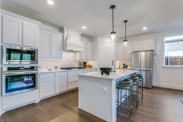 kitchen featuring appliances with stainless steel finishes, custom range hood, pendant lighting, and white cabinets