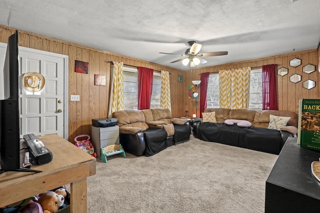 living room with ceiling fan, carpet flooring, a textured ceiling, and wood walls