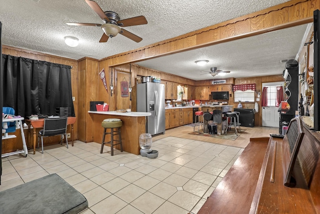 kitchen with a breakfast bar, stainless steel fridge with ice dispenser, wooden walls, ceiling fan, and kitchen peninsula