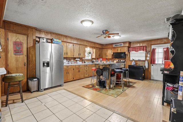 kitchen with ceiling fan, plenty of natural light, stainless steel fridge, and a breakfast bar area