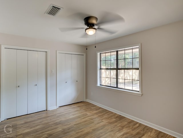 unfurnished bedroom with two closets, light hardwood / wood-style floors, and ceiling fan