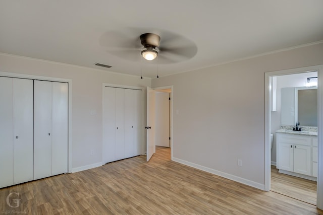 unfurnished bedroom featuring multiple closets, ensuite bathroom, ceiling fan, and light hardwood / wood-style flooring