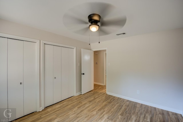 unfurnished bedroom with multiple closets, ceiling fan, and light wood-type flooring