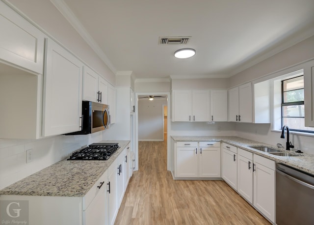 kitchen featuring appliances with stainless steel finishes, white cabinetry, sink, light stone counters, and light wood-type flooring