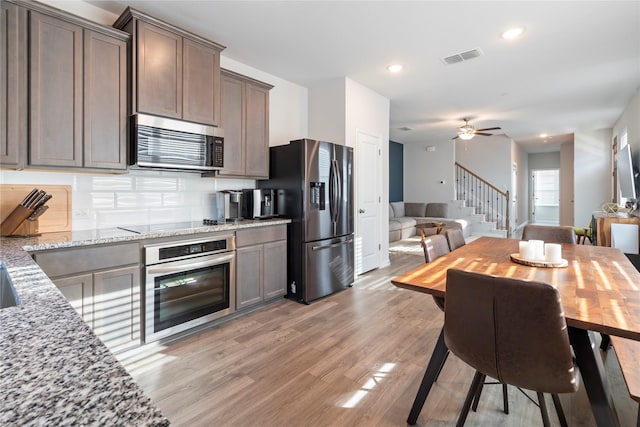 kitchen with ceiling fan, appliances with stainless steel finishes, light stone countertops, light hardwood / wood-style floors, and decorative backsplash