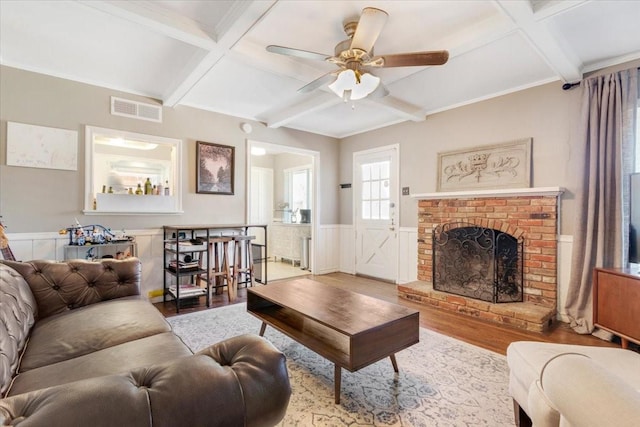 living area with a wainscoted wall, coffered ceiling, wood finished floors, visible vents, and a brick fireplace