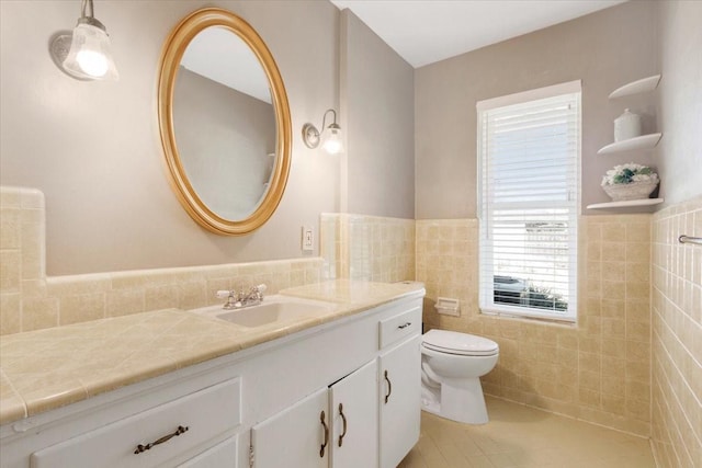 bathroom with tile walls, toilet, wainscoting, vanity, and tile patterned floors