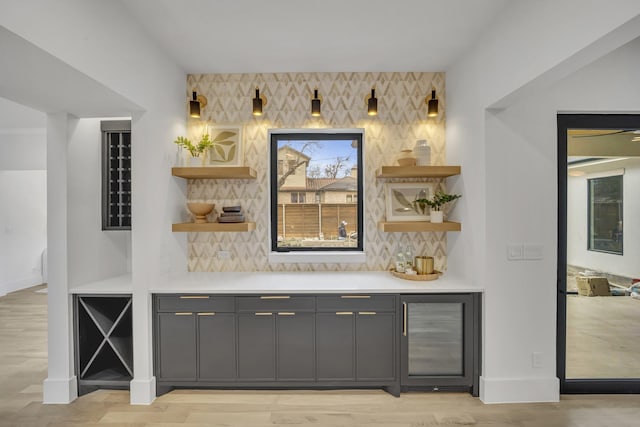 bar with tasteful backsplash, gray cabinets, beverage cooler, and light wood-type flooring