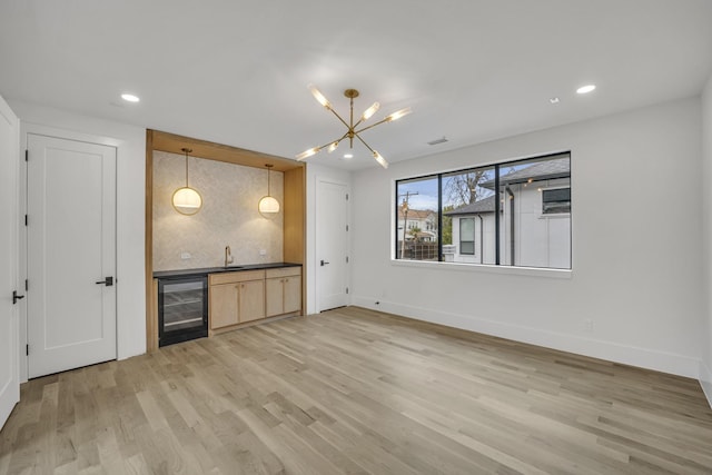 bar featuring sink, light hardwood / wood-style flooring, hanging light fixtures, beverage cooler, and light brown cabinets