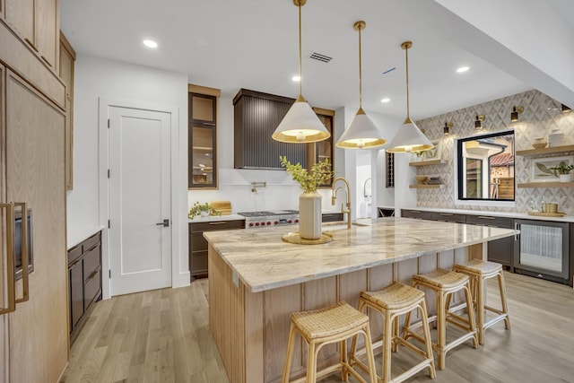 kitchen with pendant lighting, light hardwood / wood-style flooring, light stone countertops, an island with sink, and beverage cooler