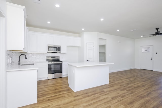 kitchen featuring sink, stainless steel appliances, white cabinets, a kitchen island, and light wood-type flooring