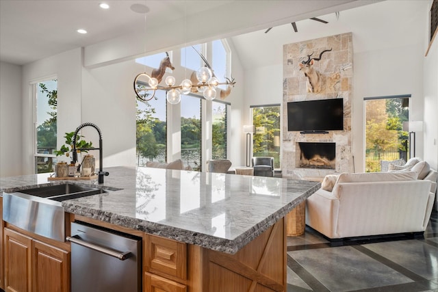 kitchen with sink, light stone counters, an inviting chandelier, a fireplace, and a kitchen island with sink