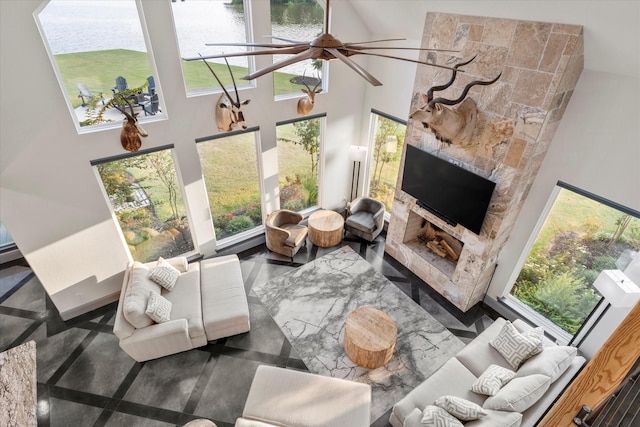 living room featuring a towering ceiling, a fireplace, ceiling fan, and a water view