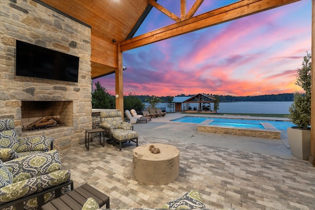 pool at dusk with a gazebo, a patio area, an outdoor living space with a fireplace, and a water view