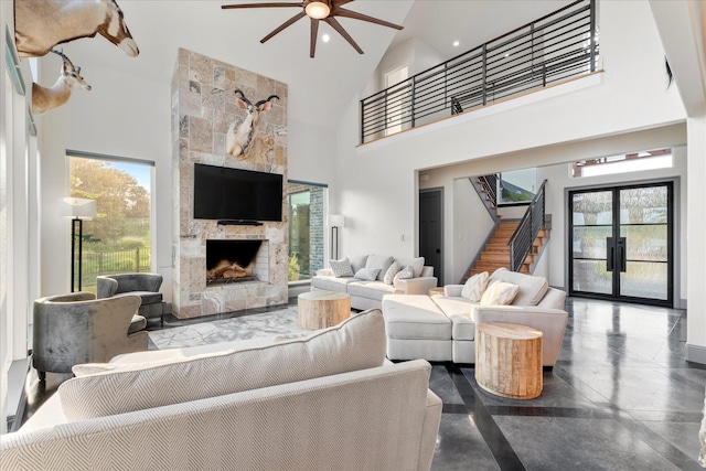 living room with ceiling fan, a stone fireplace, and a high ceiling