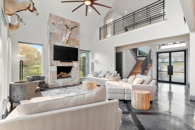 living room with a fireplace, stairs, a ceiling fan, and high vaulted ceiling