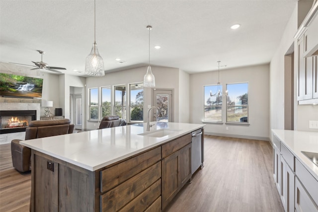 kitchen with sink, decorative light fixtures, dishwasher, a kitchen island with sink, and light hardwood / wood-style floors