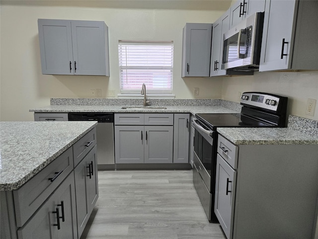 kitchen with stainless steel appliances, sink, gray cabinetry, and light hardwood / wood-style floors