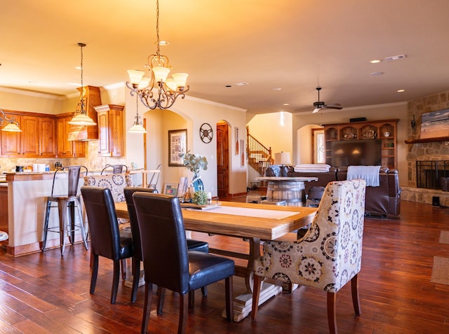 dining area with a fireplace, ceiling fan with notable chandelier, dark wood-type flooring, and ornamental molding