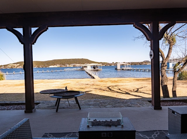 view of patio with a water view, a boat dock, and a fire pit