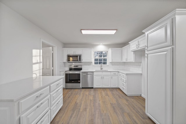 kitchen with appliances with stainless steel finishes, hardwood / wood-style floors, sink, white cabinets, and decorative backsplash