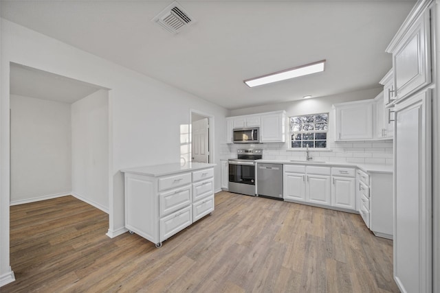 kitchen featuring sink, light hardwood / wood-style flooring, stainless steel appliances, decorative backsplash, and white cabinets