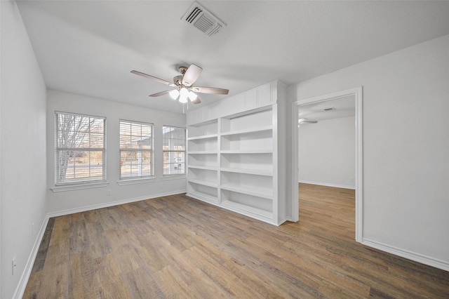 empty room featuring built in shelves, ceiling fan, and wood-type flooring