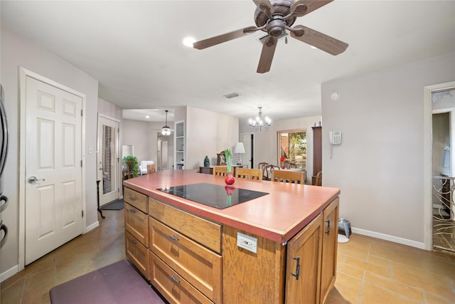 kitchen featuring black electric cooktop, hanging light fixtures, ceiling fan with notable chandelier, and a center island