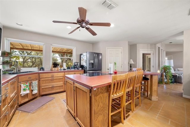 kitchen with light tile patterned flooring, sink, a kitchen bar, a center island, and stainless steel refrigerator with ice dispenser