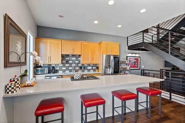 kitchen with light brown cabinetry, sink, stainless steel appliances, and a kitchen breakfast bar