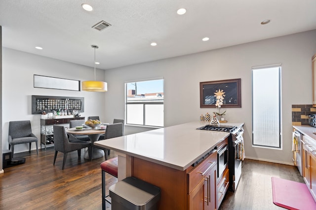 kitchen featuring pendant lighting, stainless steel range with gas cooktop, dark hardwood / wood-style flooring, and tasteful backsplash