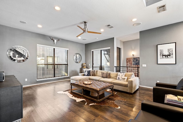 living room with a textured ceiling, dark wood-type flooring, and ceiling fan