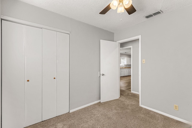 unfurnished bedroom featuring ceiling fan, a closet, light carpet, and a textured ceiling