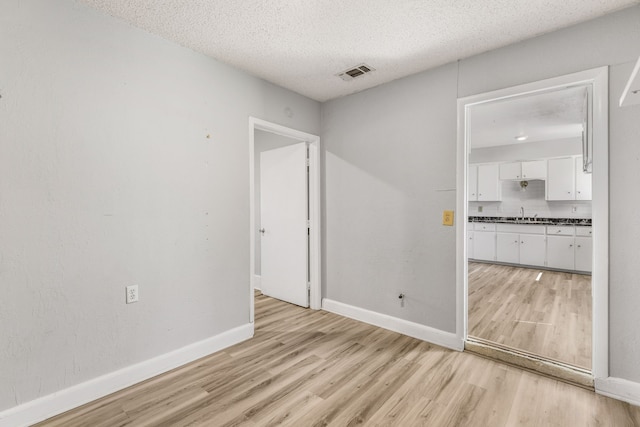 unfurnished room with light wood-type flooring and a textured ceiling