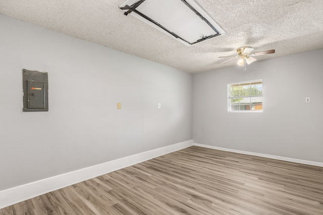 unfurnished room featuring ceiling fan, light hardwood / wood-style flooring, electric panel, and a textured ceiling